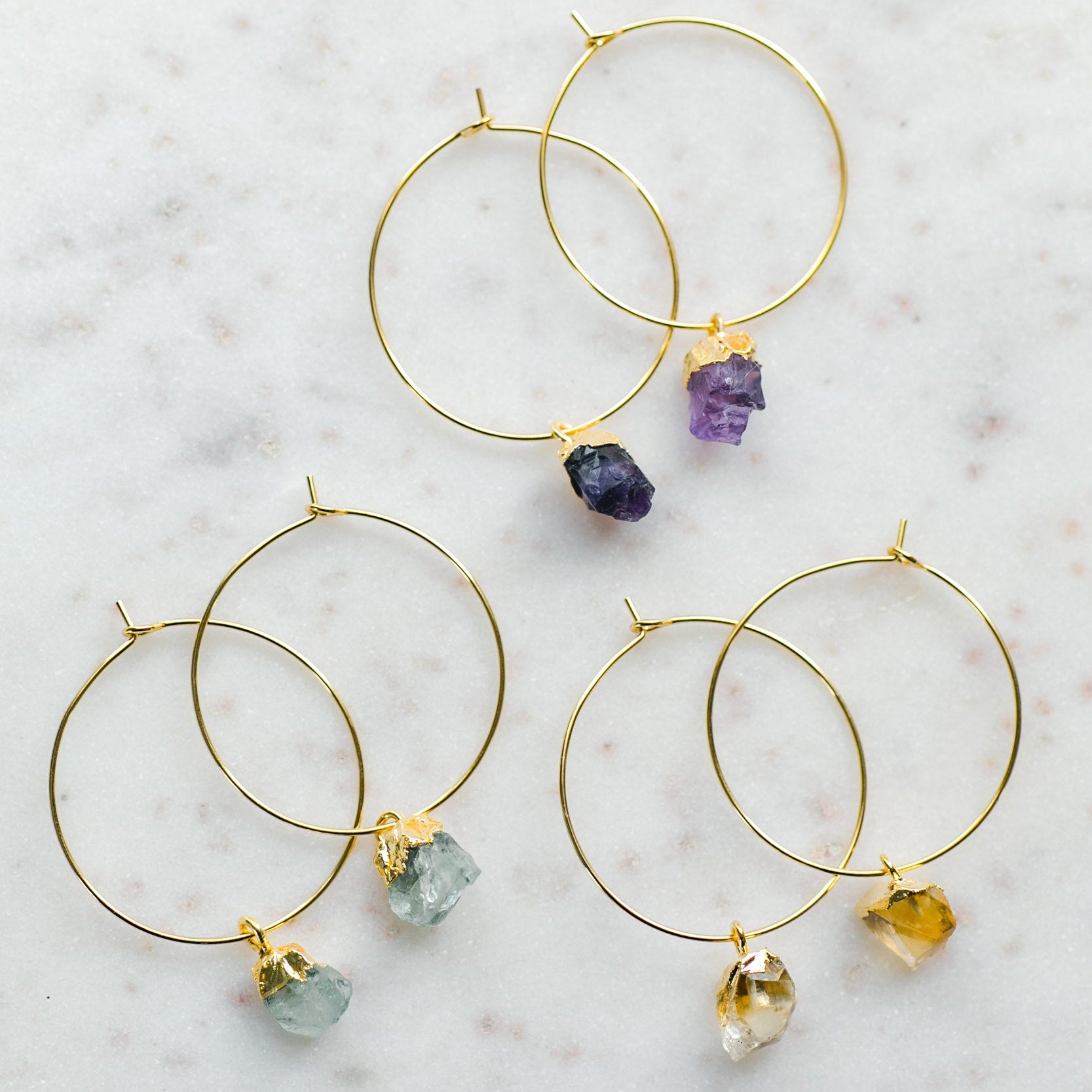 Gold hoop earrings with colorful gemstones on a marble surface